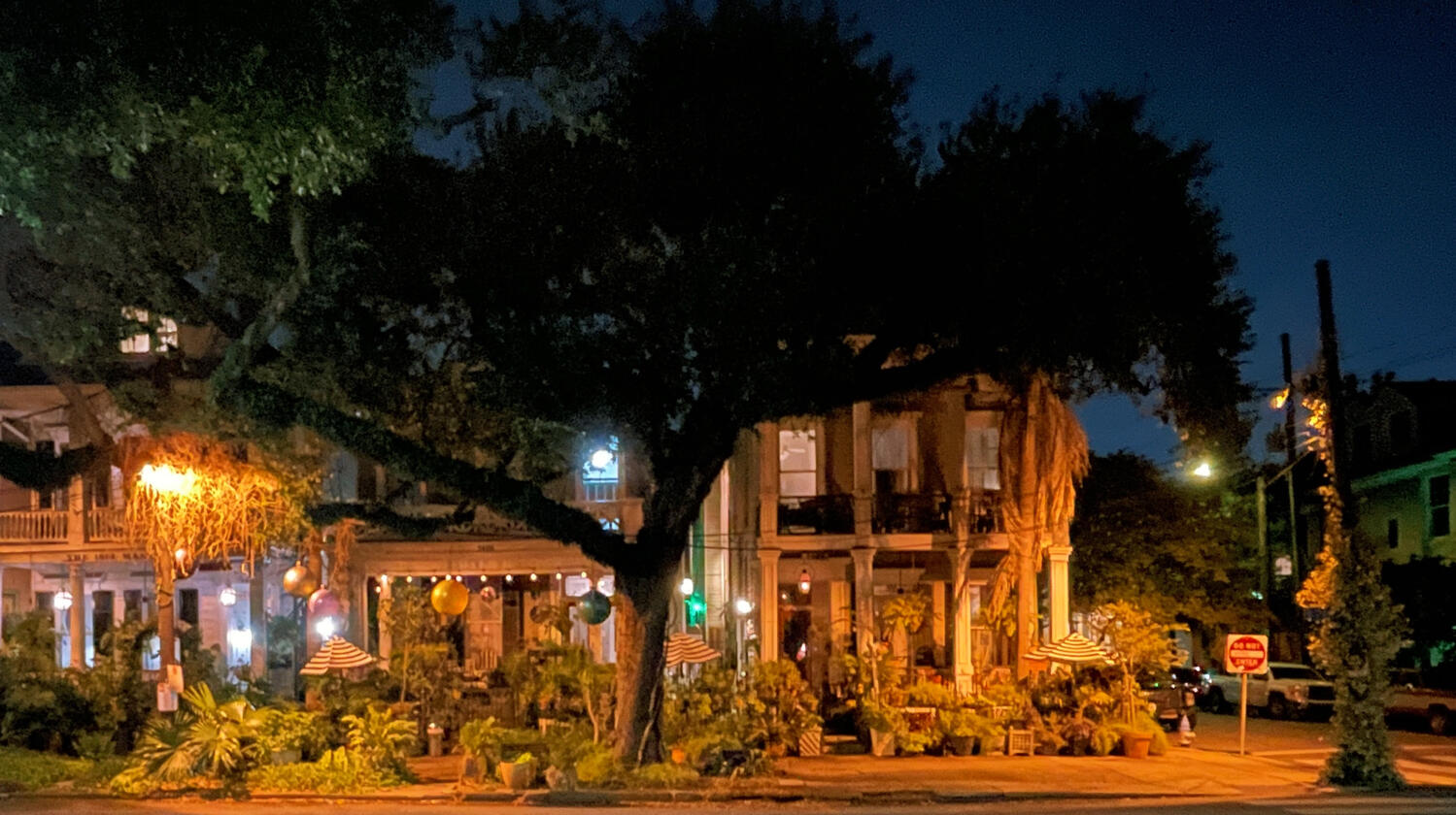 An orange-lit ramshackle house sprawling beneath an oak tree in the dark